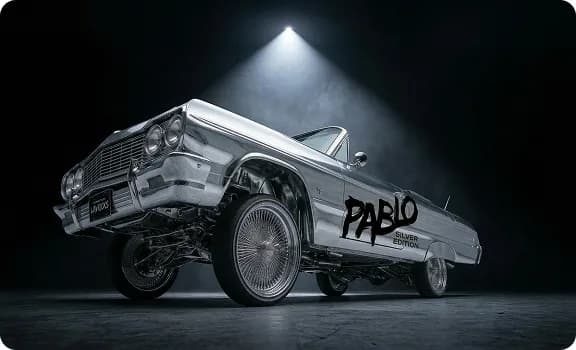 A chrome-bodied 1960s convertible lowrider, lit from above in a dark studio, with Pablo Silver Edition lettering along the rear quarter panel.
